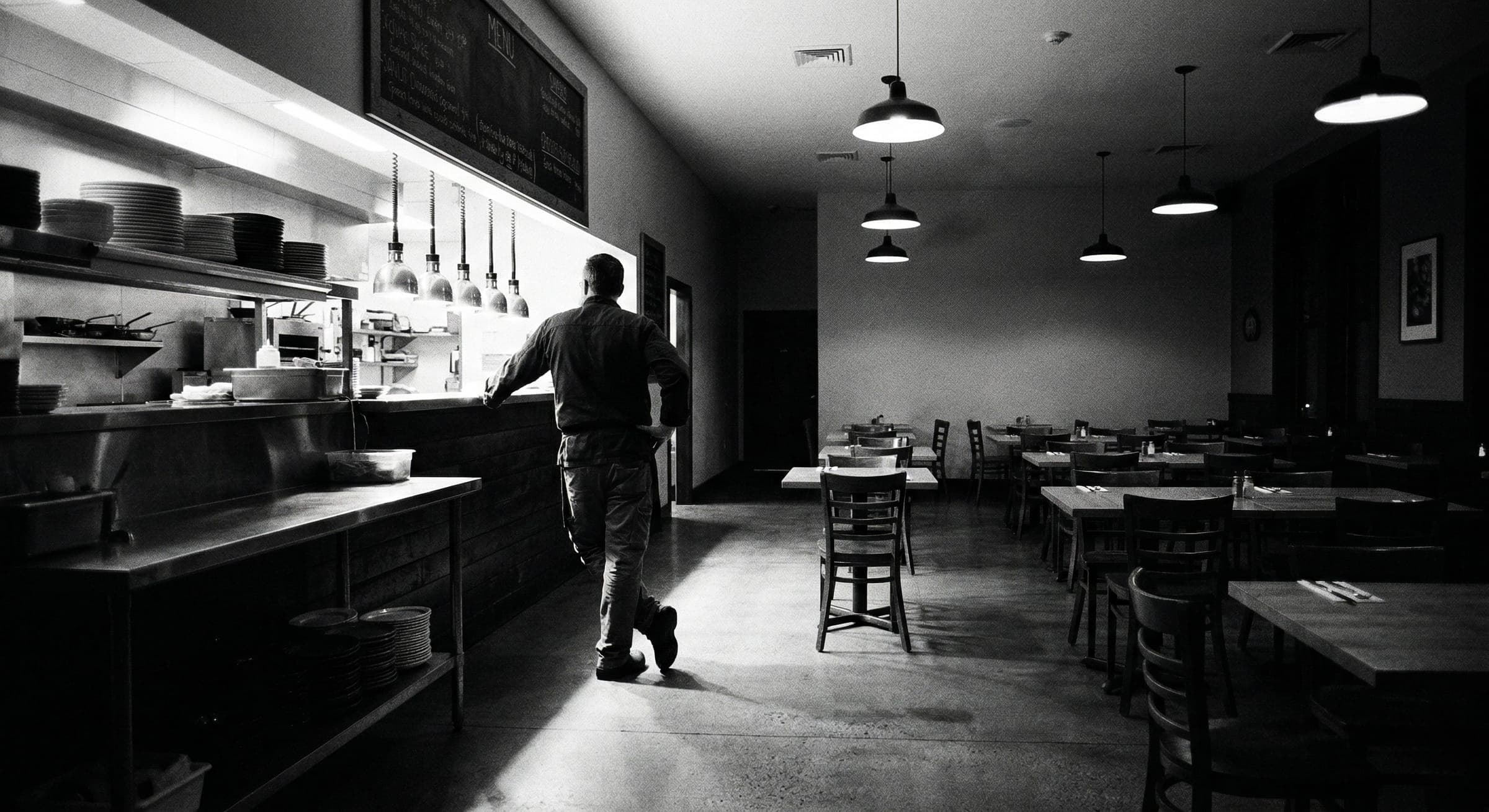 Restaurant operator standing at the pass in an empty dining room
